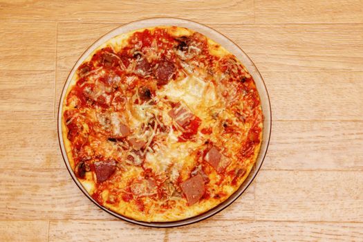 Tasty pizza with ham and sausage cooking on a wooden table.