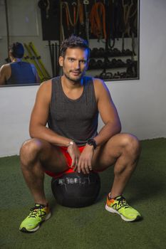 Young man sitting on a medicine ball in a crossfit gym