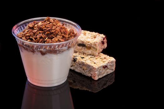Yogurt with chocolade granola and granola bar with fruits and nuts on black background with copyspace