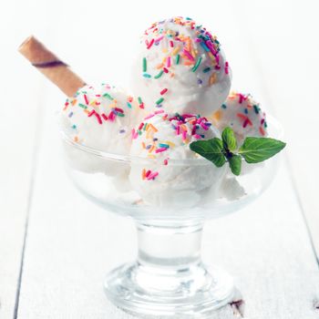 Coconut ice cream in cup with waffle on white rustic wooden background.