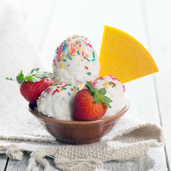 Coconut ice cream in bowl with waffle on white rustic wooden background.