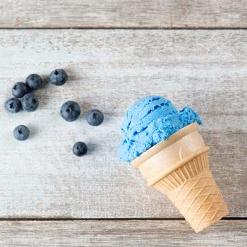 Top view blue ice cream in waffle cone with blueberry fruit on rustic wooden background.