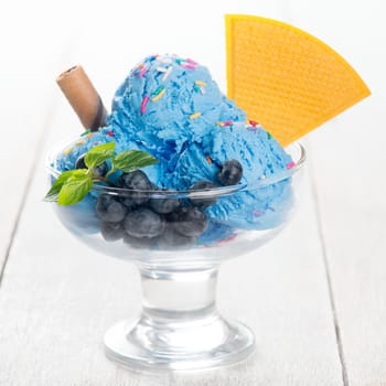 Blue ice cream in cup with blueberry fruits on white rustic wooden background.