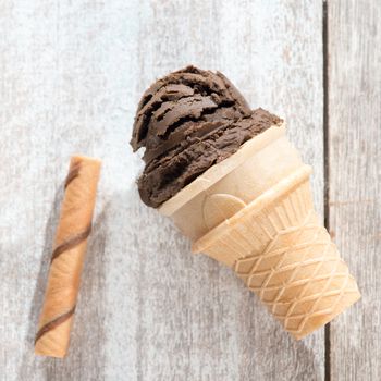 Top view chocolate ice cream in waffle cone on bright wooden background.