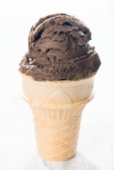 Brown ice cream in waffle cone on wooden background.