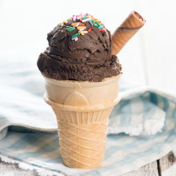 Chocolate ice cream in waffle cone on bright background.