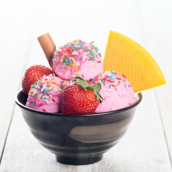 Pink ice cream in bowl with strawberry fruits on white rustic wooden background.