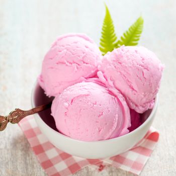 Strawberry ice cream in bowl on white wooden background.