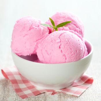 Pink ice cream in bowl on white wooden background.