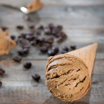 Close up brown ice cream in cone and coffee beans on old rustic vintage wooden background.