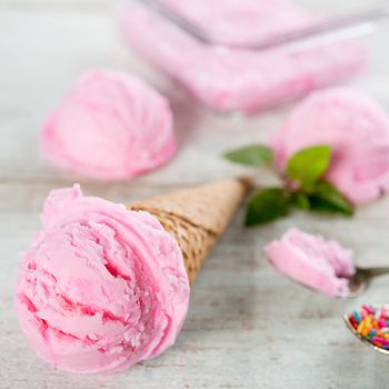Strawberry ice cream waffle cone on wooden background close up.