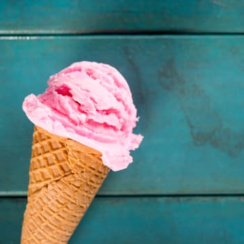 Top view strawberry ice cream waffle cone on blue wooden background, close up.