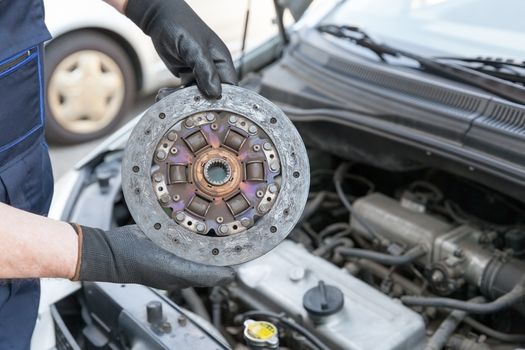 Auto mechanic wearing protective work gloves holds old clutch disc over  a car engine