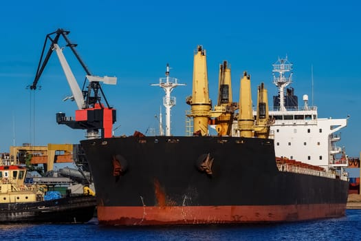 Black cargo ship mooring at the port with tug ship support