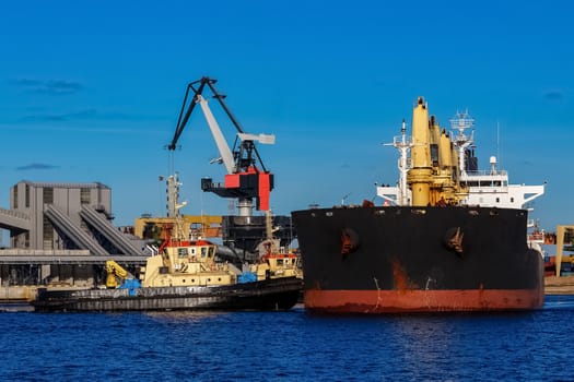 Black cargo ship mooring at the port with tug ship support