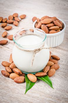 Almond milk and dry almond nuts with green leaf on a wooden table.