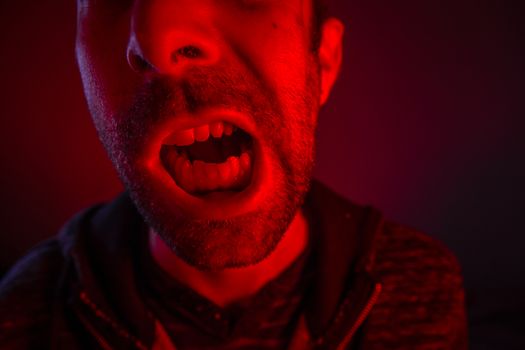 Man with angry facial expression screaming out loud. Close up portrait of a man shouting with mouth wide open.