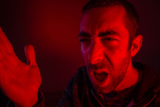 Man with angry facial expression screaming out loud and waving with his hand. Close up portrait of a man shouting with mouth wide open.
