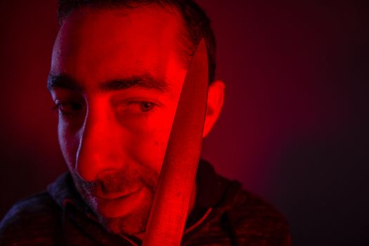 Closeup of sinister man looking at a knife that he holding.