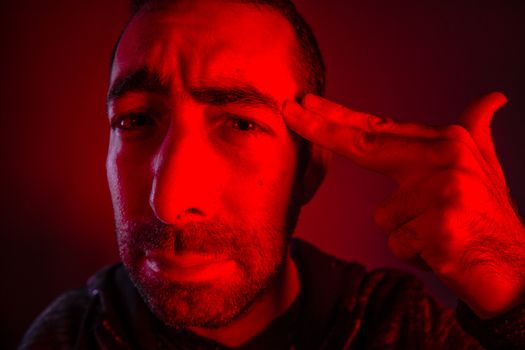 Closeup of sad young man committing suicide with finger gun gesture.