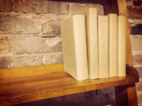Books in paper covers on a wooden shelf, near a brick wall. Retro style image.