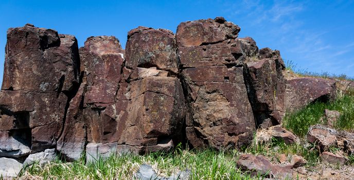 Red desert rocky hillside with rough cracked stones and grass