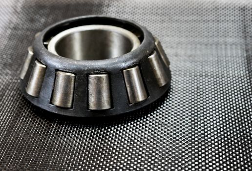 Antique automotive tapered roller bearing on plain weave carbon fiber.