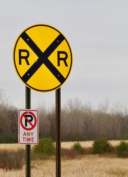 A bright yellow circular railroad crossing sign shows against a rural background.