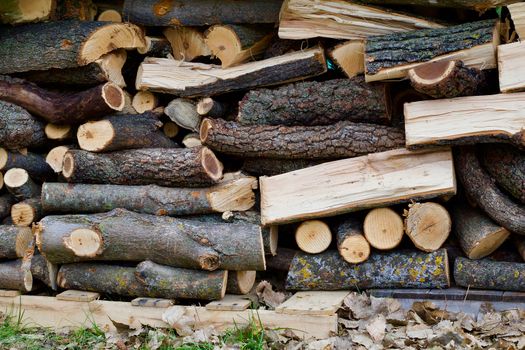 Stacked, cut and split wood pieces are stacked neatly by the autumn leaves.