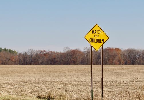 A bright yellow watch for children warning sign shows against a rural background.