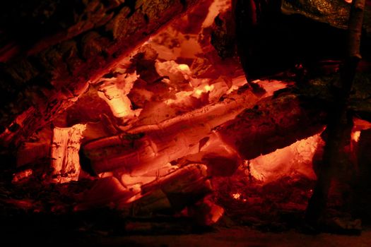 A closeup of bright red and yellow wood coals glow in the night.