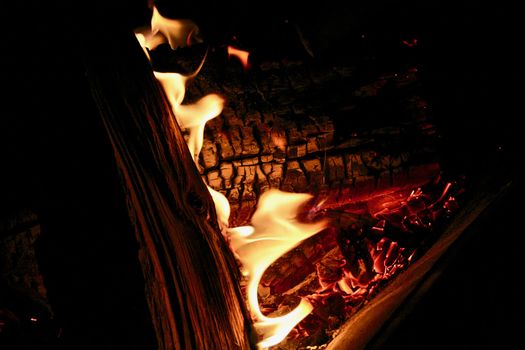 Dancing flames appear on the charred wood amidst the glowing coals.