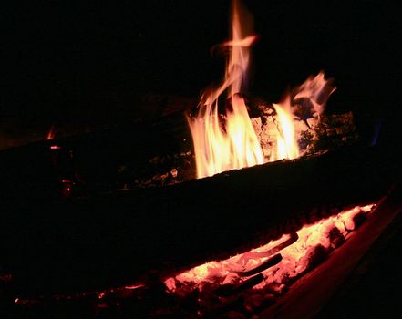 Flames lick up from the burning wood in the night camp fire.