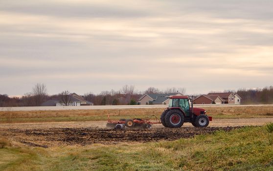 A red tractor pulls a disk across a harvested field.