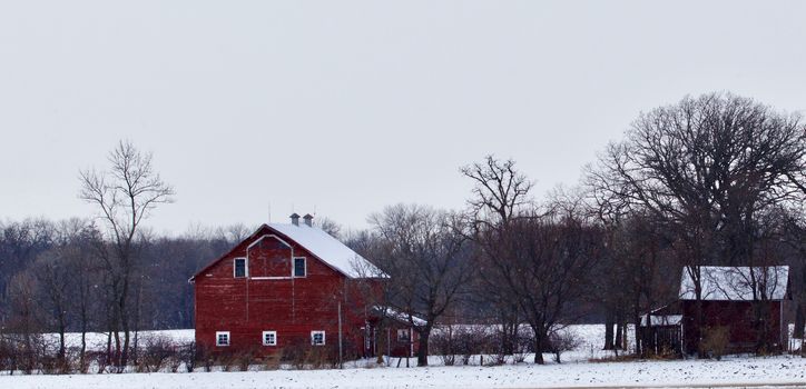 A valleyside red barn appears on a snowy day.