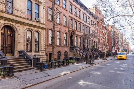 Scenic tree lined street of historic brownstone buildings in the West Village neighborhood of Manhattan in New York City, NYC USA. Traditional yellow taxi car driving along street.