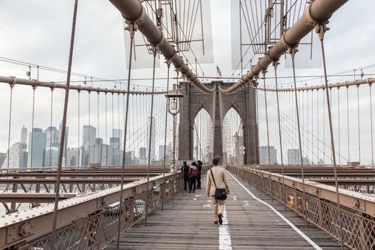 Man walking on pedestrian path across Brooklyn bridge. New York City Manhattan downtown with skyscrapers over East River panorama as seen from Brooklyn bridge.