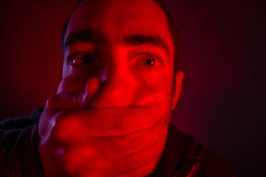 Closeup of a mans hand covering a man mouth with terrified facial expression.