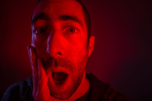 Man with surprised facial expression with opened mouth. Close up headshot portrait of shocked man with his hand on the face.