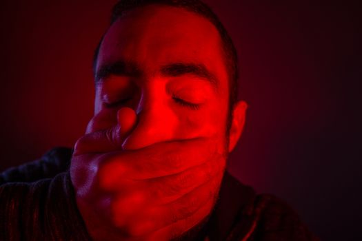 Closeup of a mans hand covering a man mouth with terrified facial expression.