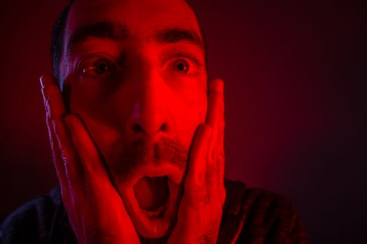 Man with surprised facial expression with opened mouth. Close up headshot portrait of shocked man with his hand on the face.