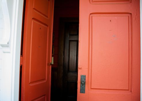 Old wood red double doors leading in to a dark hall with another set of doors visible inside