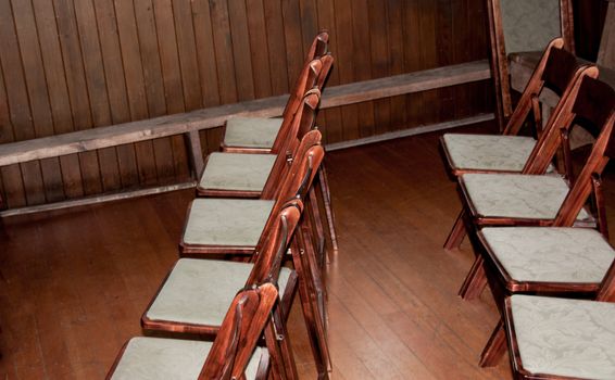 Old wooden folding chairs with white cloth seats on a hardwood floor and wooden walls