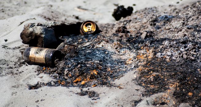 Garbage on a beach camp fire left over from a party with bottles and cans