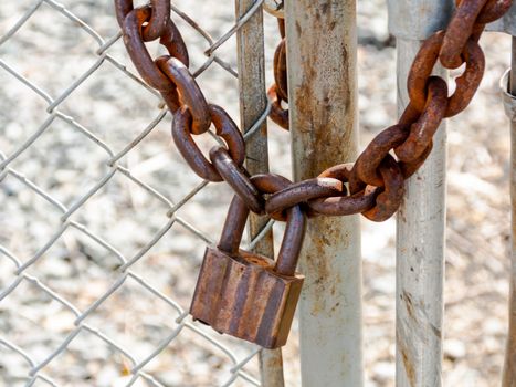 Old rusty heavy duty pad lock and chain on a fence and gate junction in the say