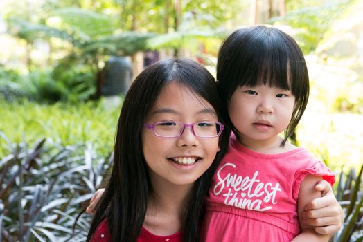 Two cheerful Asian little girls in a summer park.