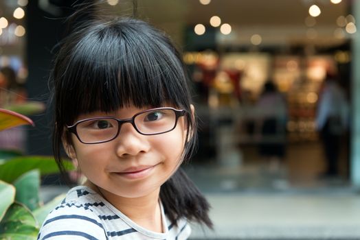 Cute little Asian Chinese girl with glasses in park smiling