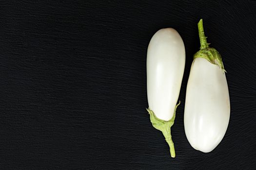 White eggplant on a black stone surface. Top view. Copy space.