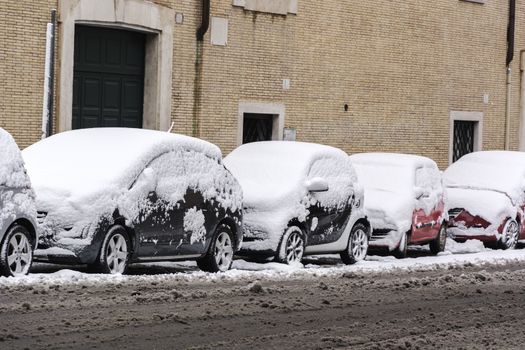 cars parked in a row covered by snow with already melted snow on the road