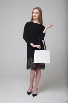 Young beautiful long-haired girl in black dress poses with white paper bag for shopping